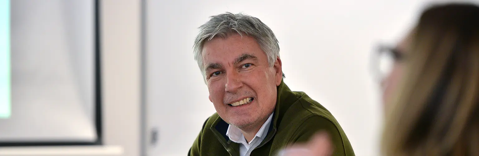 A professionally dressed man sat in a classroom environment participating in group work