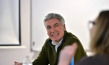 A professionally dressed man sat in a classroom environment participating in group work