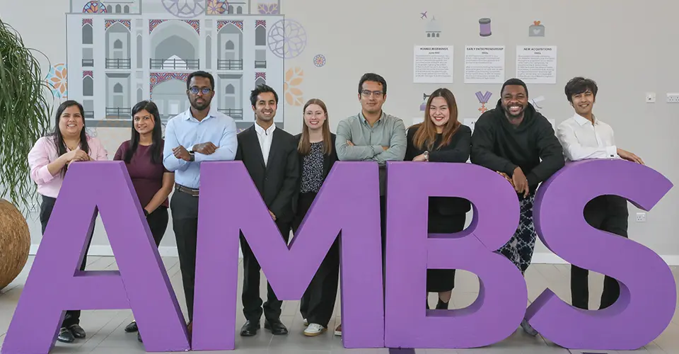 Nine full-time MBA student council members posing next to large purple AMBS letters.