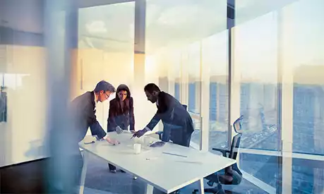Three people meeting in a glass office at the top of a skyscraper