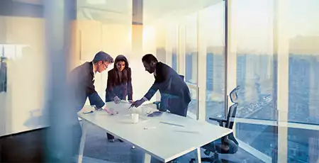 Three people meeting in a glass office at the top of a skyscraper