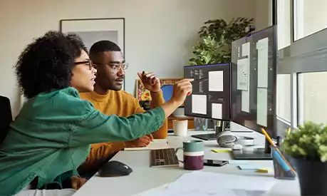 Two colleagues looking at multiple computer screens