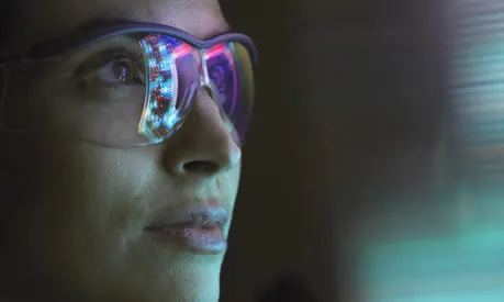 A person looking at a screen with glasses on. We can see the reflection of the screen in the glasses.
