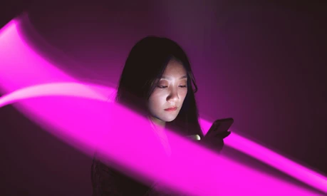 A woman looking at her smartphone whilst being surrounded by a stream of purple light.