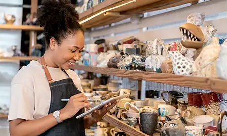 A black woman holding an iPad in a small shop.
