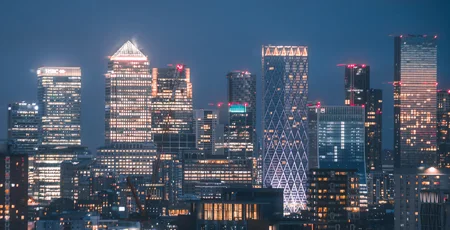 An aerial view of multiple tall buildings in the Canary Wharf skyline at night