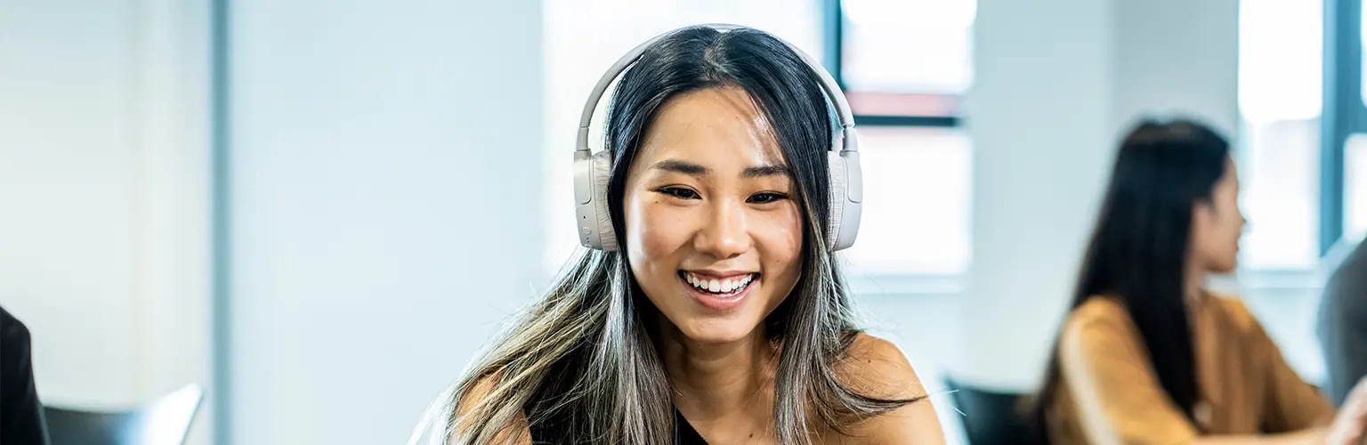 Alliance MBS student smiling while studying with headphones in a classroom.