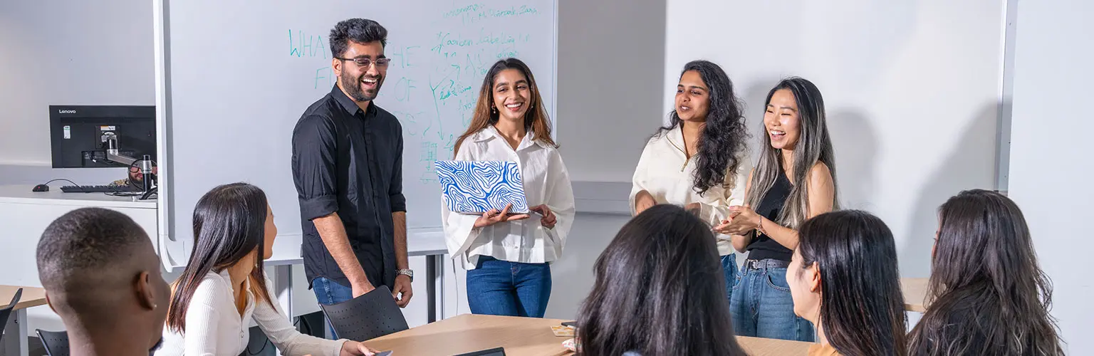 A group of students give a presentation in a classroom, smiling and engaging with their classmates.