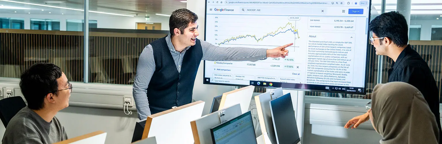 Students in a classroom discuss data displayed on a large screen.