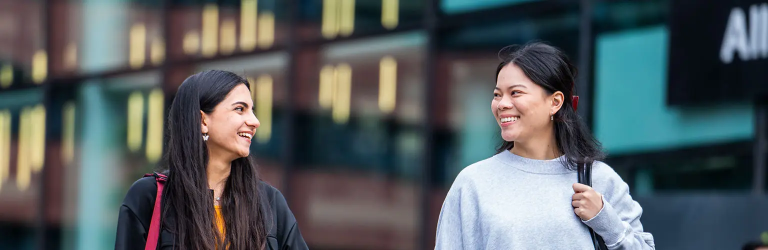 Two students walking outside Alliance MBS, smiling and talking together.