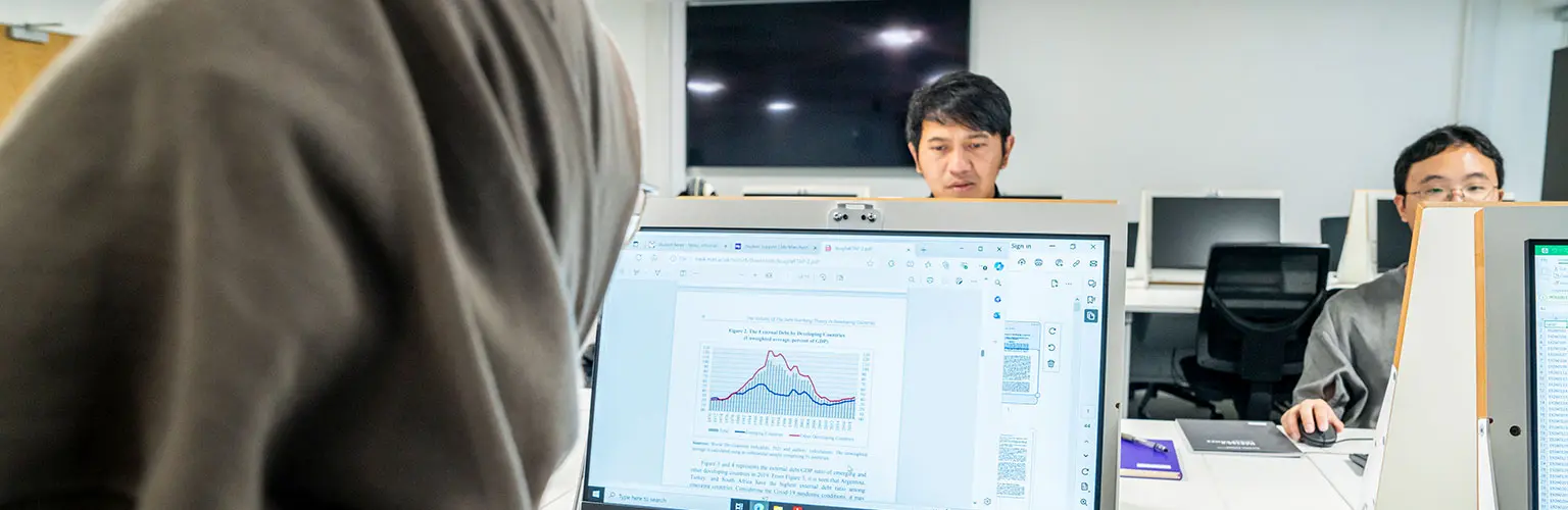 Students working at computer screens in a classroom, analysing financial graphs and data.