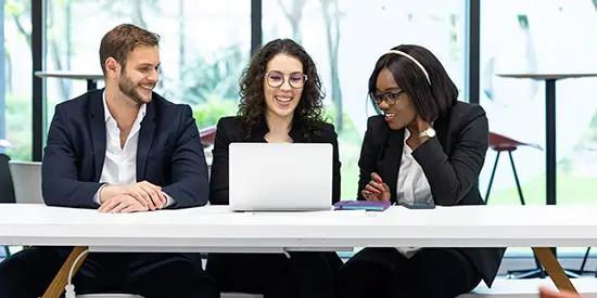 Three students chatting while looking at a laptop