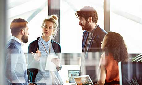 Four people standing together in an office having a discussion