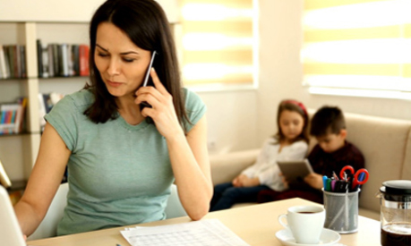 a woman working from her home office on her phone with her children learning on a tablet