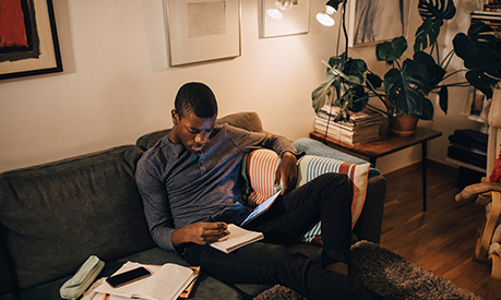 High angle view of a man using digital tablet while studying on sofa at home