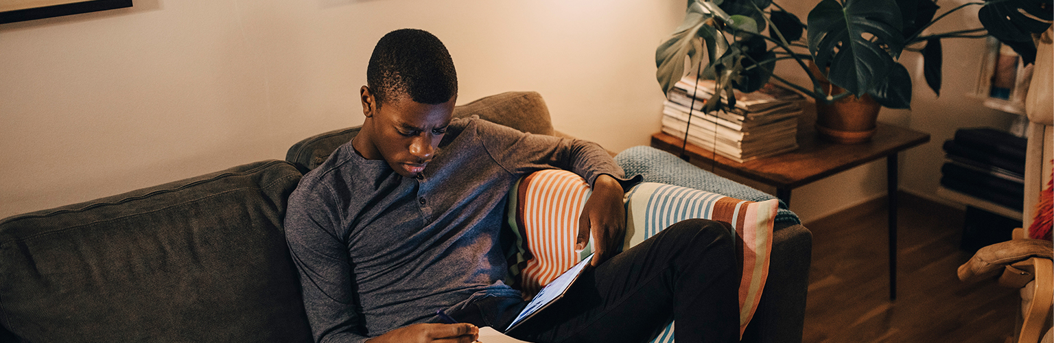 High angle view of a man using digital tablet while studying on sofa at home