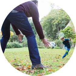 a child in the garden kicking a football with his dad