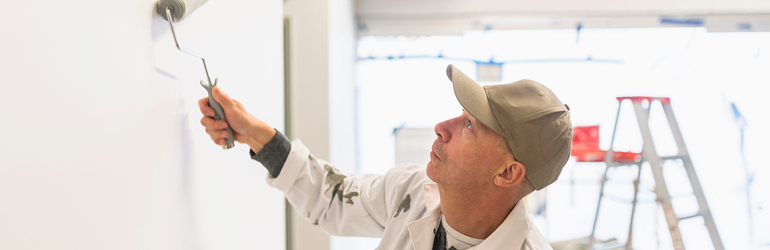 A self employed painter painting a white wall with a roller