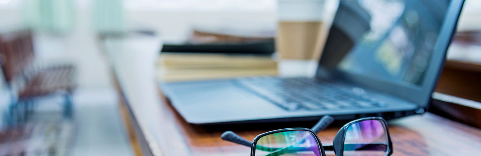 A pair of glasses and a laptop on a desk in an office