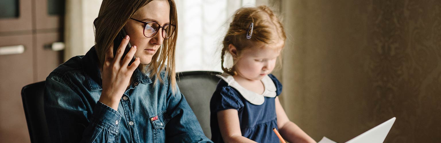 A woman working on her desk with her child next to her