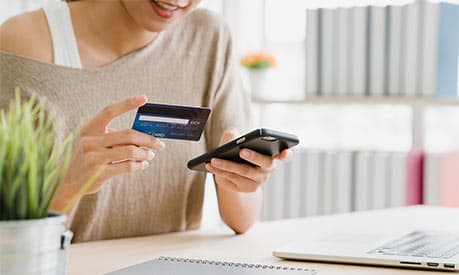 A woman holding a phone in one hand and a credit card in the other