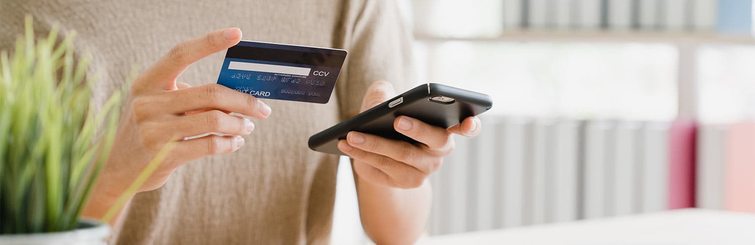 A woman holding a phone in one hand and a credit card in the other