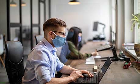 A man sitting at a desk wearing a mask