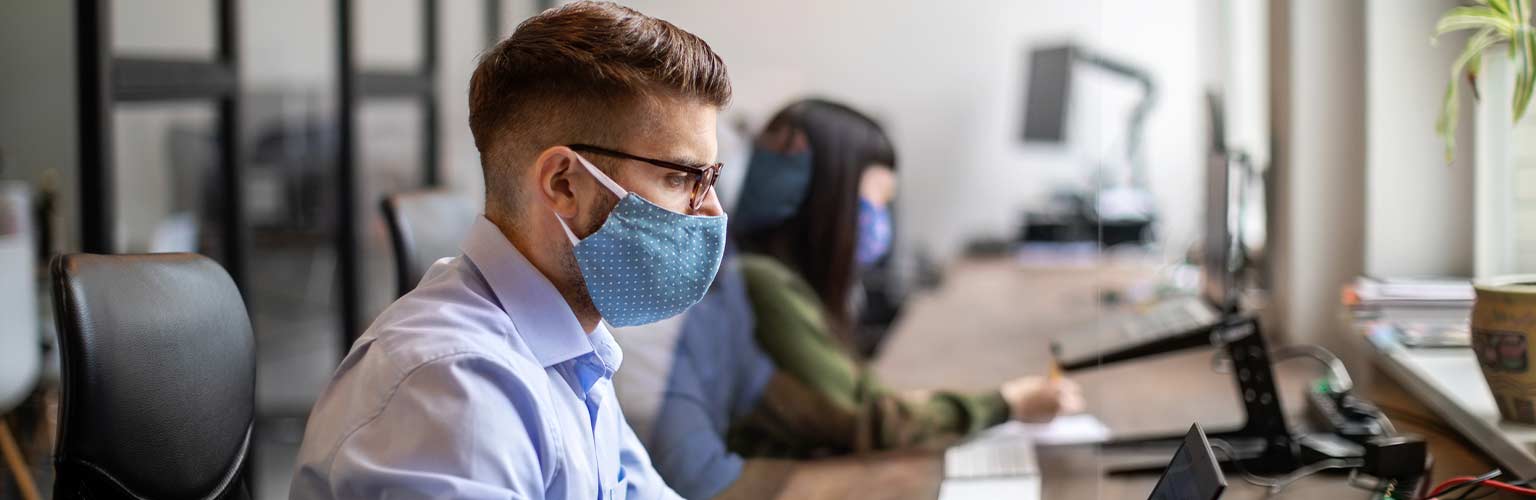 A man sitting at a desk wearing a mask