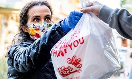 A woman in a mask giving a bag of food shopping to somebody else