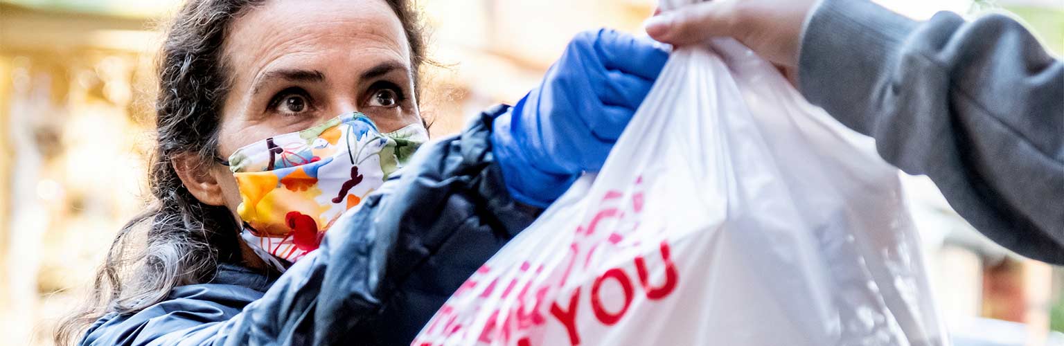 A woman in a mask giving a bag of food shopping to somebody else