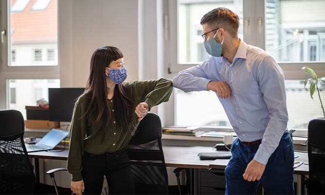 Colleagues in an office elbow bumping with masks on