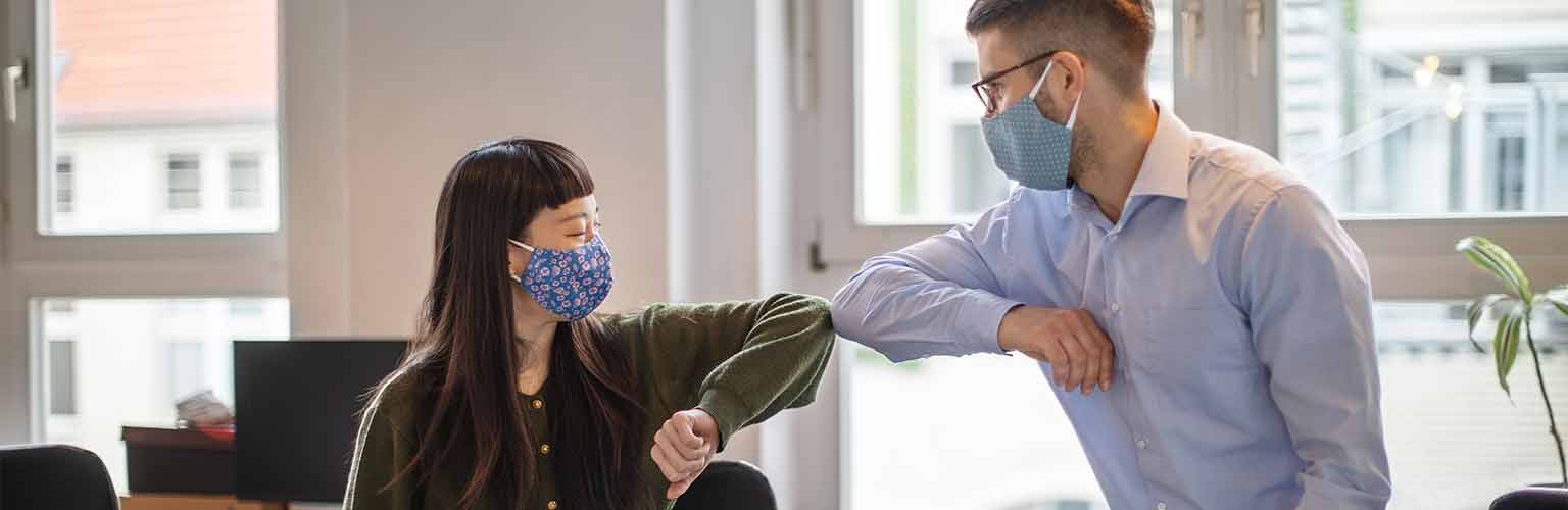 Colleagues in an office elbow bumping with masks on