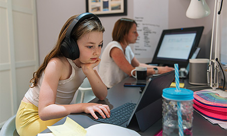 A young girl working on a laptop on the same desk as her mother