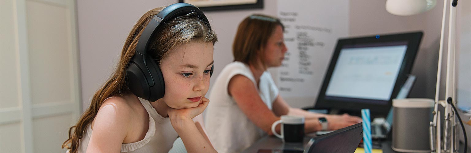 A young girl working on a laptop on the same desk as her mother