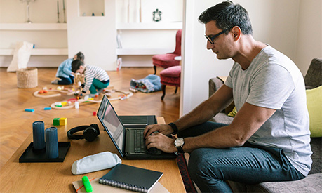 Father typing over laptop while children playing in background at home