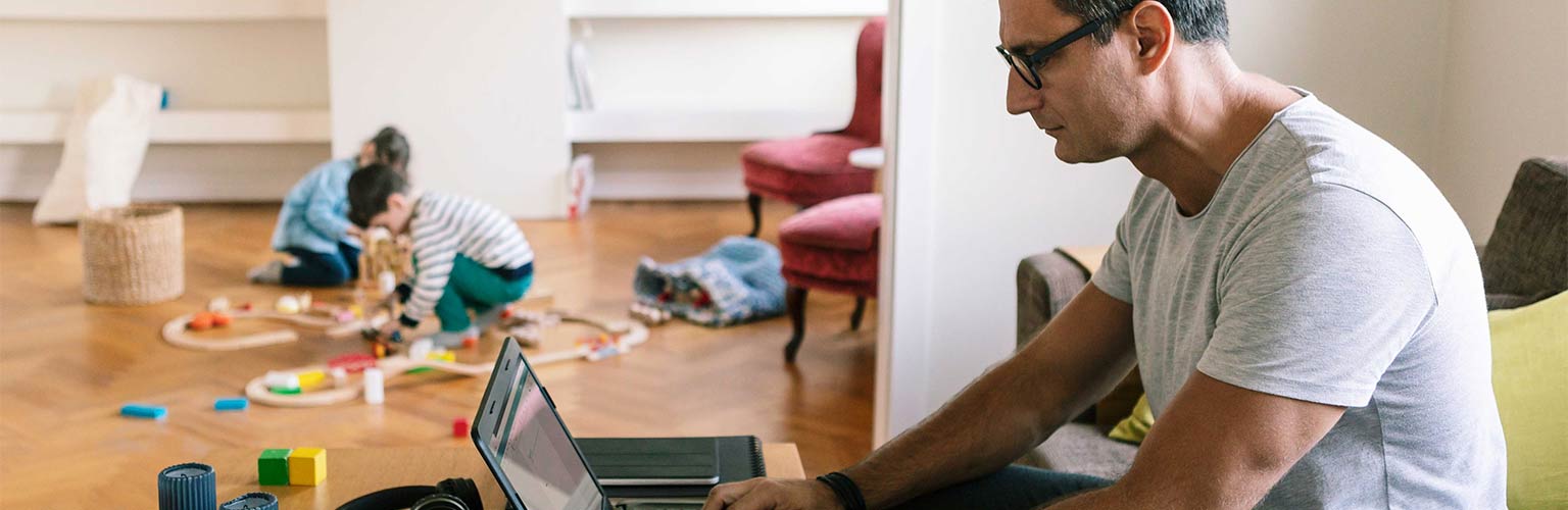 Father typing over laptop while children playing in background at home