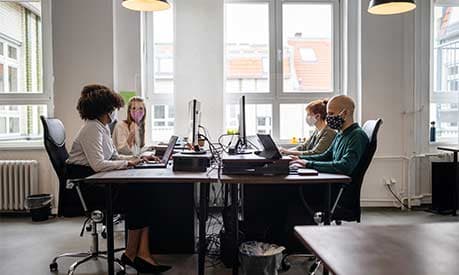 Four people in an office sat at a desk with face masks on