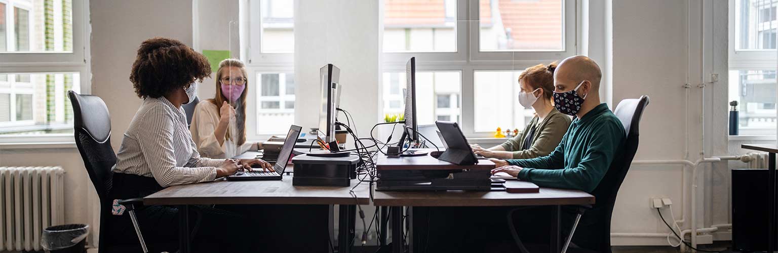 Four people in an office sat at a desk with face masks on