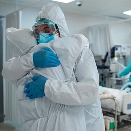 two healthcare workers embracing on a ward in full ppe