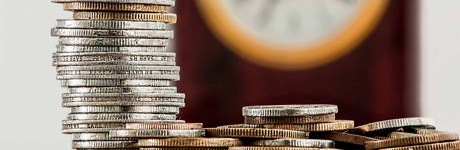 a pile of silver coins in the foreground and a clock in the background
