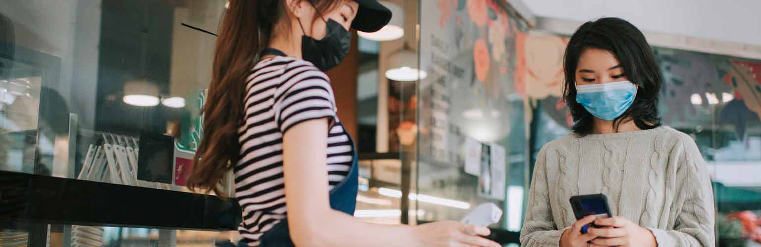 A woman wearing a mask using her phone to log in to a track and trace app