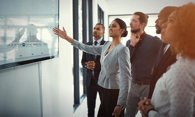 A woman presenting to her colleagues pointing to a screen