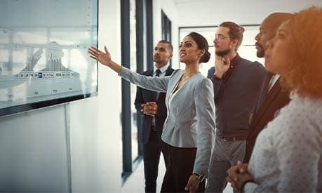 A woman presenting to her colleagues pointing to a screen