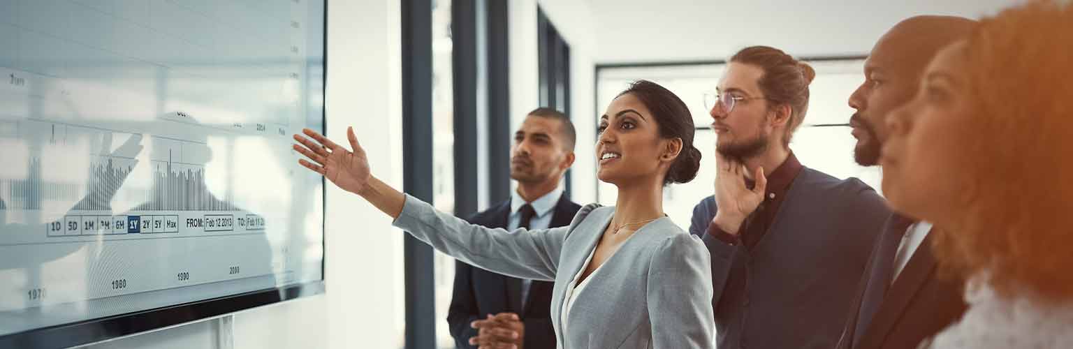 A woman presenting to her colleagues pointing to a screen