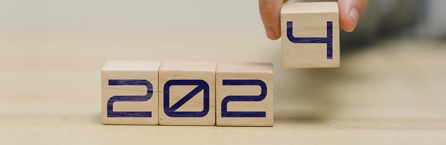 A hand places a cube containing the number '4' spelling out the year 2024 in wooden blocks