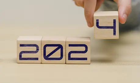 A hand places a cube containing the number '4' spelling out the year 2024 in wooden blocks