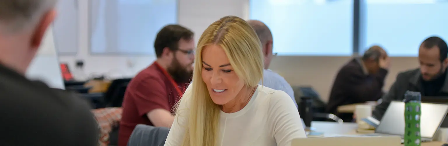 A female professional leader sitting around a table as part of a group in a classroom.