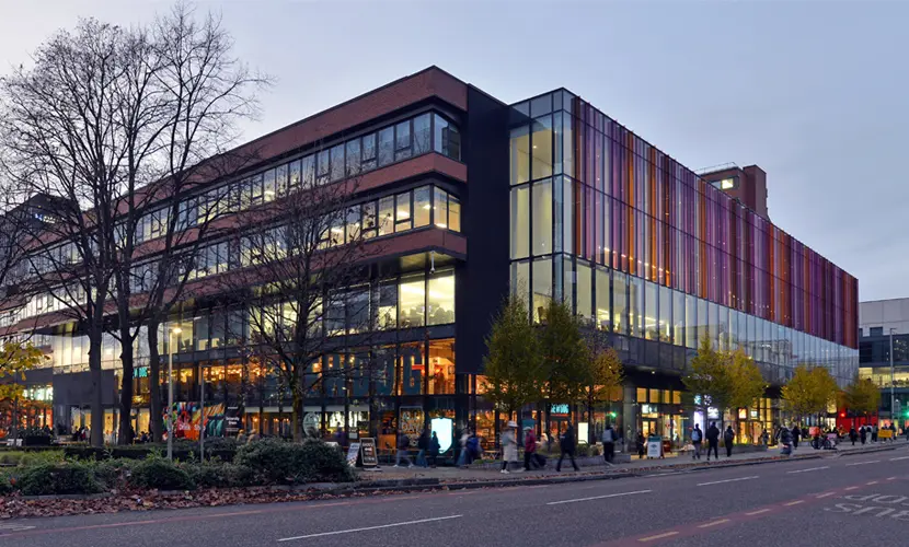 Alliance Manchester Business School building with a tree in front of it in the evening light.