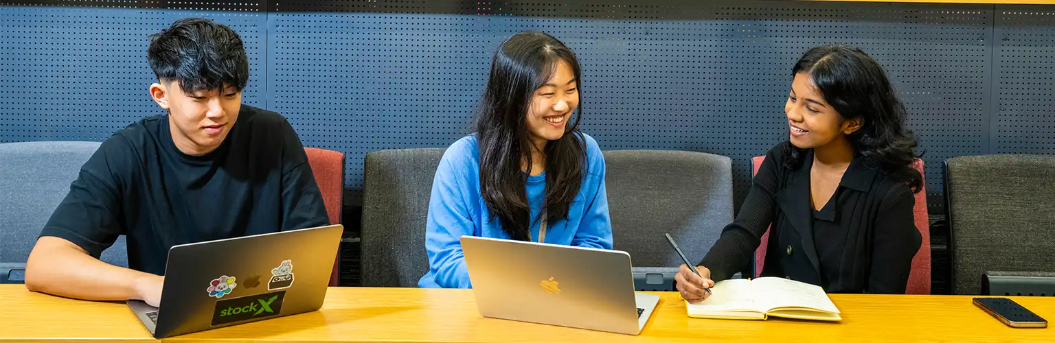 Three master's students working on laptops in a lecture theatre.