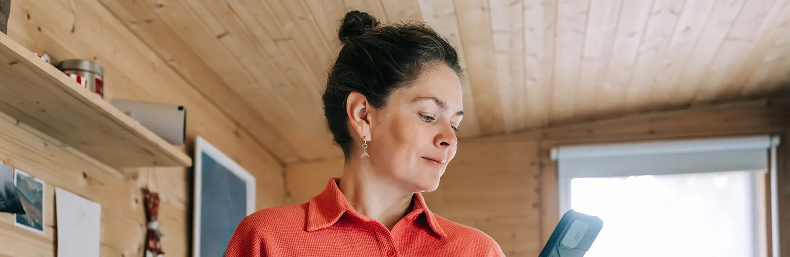 Woman enjoying morning coffee and checking her phone in rustic kitchen.